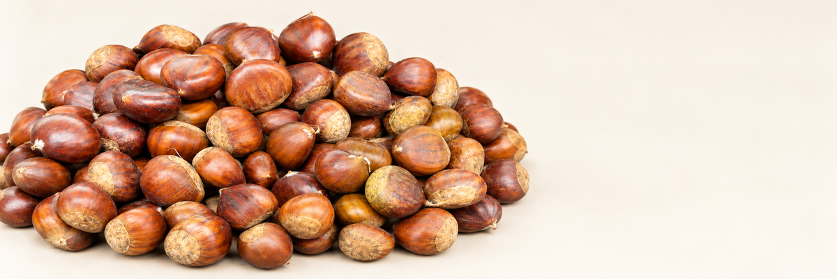 Fresh whole Portuguese chestnuts on a clean warm ivory surface